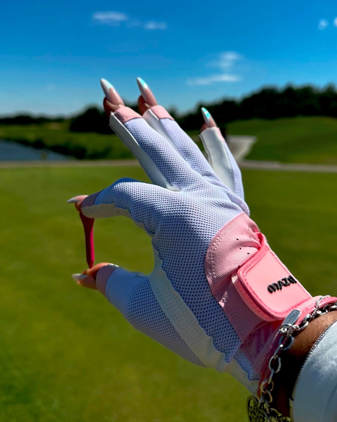 Woman's gloved hand holding a golf tee on a sunlit course
